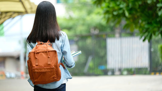 Young girl with straight black hair and tan backpack walking outside near school