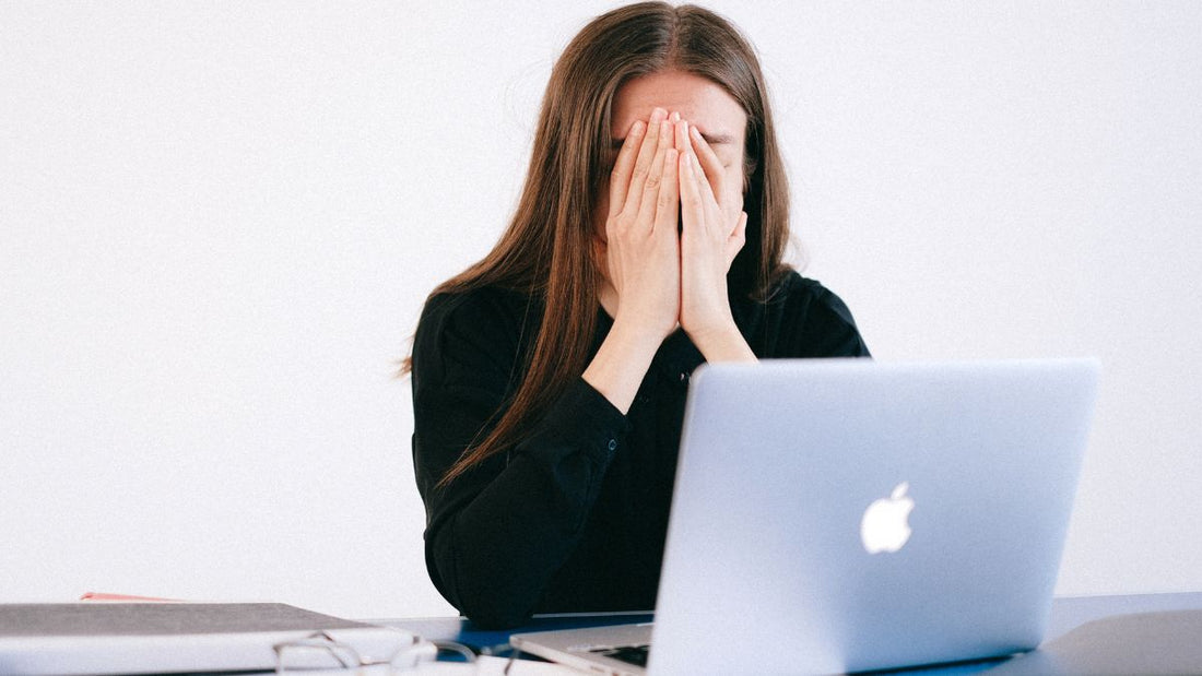 Brunette woman sitting in front of macbook with hands in front of face looking very stressed