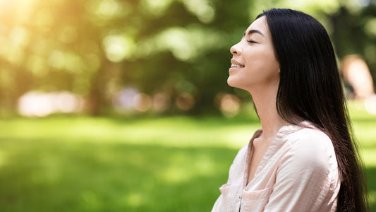 Woman with black hair outside in nature siling with her eyes closed