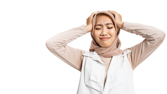 a woman appearing stressed while holding her head wearing a head covering and a white background