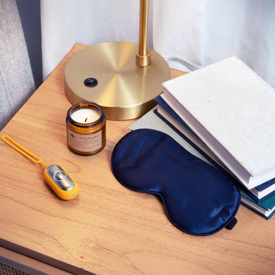 Bedside table setup with The Chill Pill, sleep mask, aroma candle, and books for a relaxing night.