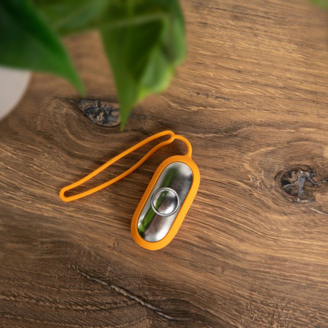 The Chill Pill on a rustic wooden table, showcasing its sleek, modern design with an orange strap.